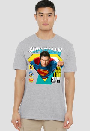Young man wearing gray T-shirt with colorful Superman graphic showing flying hero and text "You'll believe a man can fly."