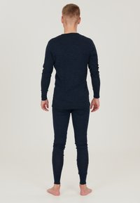 Mörkblå långärmad topp och matchande figurnära byxor i ett mjukt, texturerat material. Enkelt design, ingen synlig mönster eller hårdvara.
