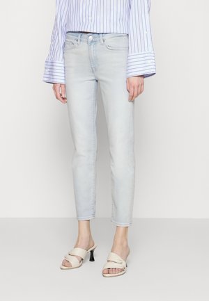 Lichtblauwe denim jeans, slim-fit, boven de enkel geknipt. Gepaard met nude hoge hak sandalen en een gestreept overhemd met lange mouwen.