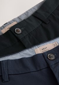 Zwei Paar gerade geschnittene Hosen in Schwarz und Marineblau mit Knopfverschluss und sichtbaren inneren Bundetiketten.