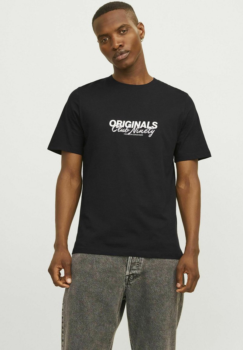 Camiseta de algodón negra con el texto en blanco y en negrita "ORIGINALS Club Winery" en el frente, cuello redondo y mangas cortas, combinada con jeans grises.