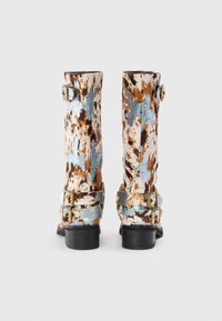 Botas de cuero moteadas en marrón y blanco con un brillo iridiscente, que presentan dobles hebillas en tono dorado en el tobillo y un tacón negro.