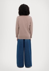 Beige knit sweater with dropped shoulders, paired with wide-leg blue denim pants featuring a frayed hem. Plain background.