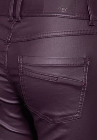 Burgunderröda läderliknande byxor har en figurnära design, slät textur och två bakfickor med kontrasterande sömmar och knappdetaljer.