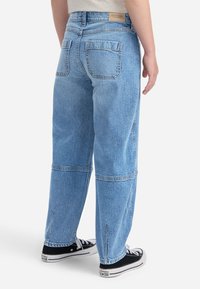 Vaqueros de denim de color azul claro con un corte relajado, cinco bolsillos, costuras visibles y un dobladillo ligeramente deshilachado, combinados con zapatillas negras.