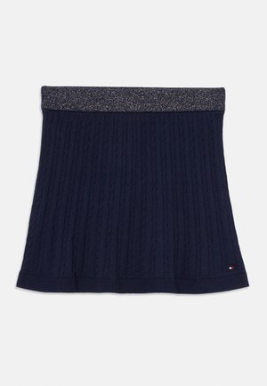 Jupe tricotée bleu marine avec texture côtelée, accentuée par une taille métallique argentée. Présente un logo de marque discret à l'ourlet.