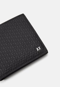 Black wallet made of textured material, featuring a raised pattern and a silver logo accent. Compact design with sharp edges.
