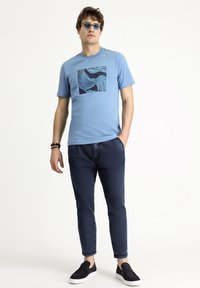 Camiseta de algodón azul claro con un estampado gráfico geométrico en azul marino, combinada con pantalones azul marino oscuro y zapatos negros tipo slip-on.