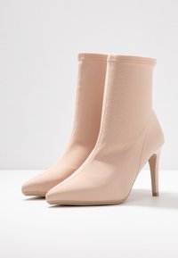 Nude wysokie botki na obcasie z ostro zakończonym noskiem, wykonane z gładkiego materiału, charakteryzujące się bezszwowym, dopasowanym krój i smukłym obcasem w stylu szpilki.