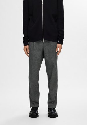Zip-up, black knit cardigan over gray plaid trousers. Trousers feature a relaxed fit. Black shoes with textured detail. Simple, modern design.