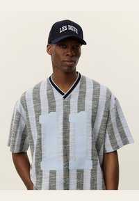 Camisa de mangas curtas cinza com riscas, com o número azul "11" na frente, design de decote em V, e um boné azul-marinho com letras brancas.