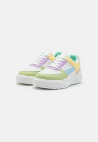 Baskets colorées avec un mélange de matériaux synthétiques blancs, lavande, jaunes et verts. Semelle épaisse blanche avec des détails texturés.