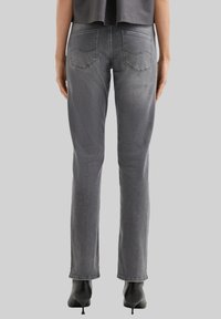 Vaqueros de mezclilla gris con un corte slim, que cuentan con dos bolsillos traseros, un sutil patrón de desgaste y un diseño de pierna recta. Los zapatos son tacones negros.