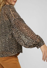 Camicia nera trasparente con un motivo a macchie in beige e marrone. Presenta maniche a palloncino e una vestibilità morbida, con una leggera lucentezza.