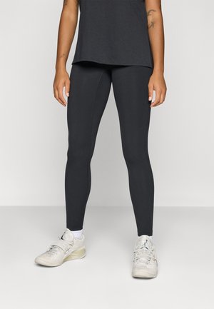 Leggings noirs avec une texture lisse, taille haute et design ajusté. Portés avec un haut noir ample et des chaussures de sport de couleur claire.