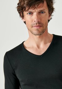 Zwarte lange mouw V-hals shirt van een zachte, rekbare stof, met een aansluitend ontwerp en een gladde textuur. Minimale stikdetails.