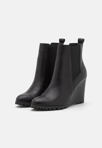 Wedge ankle boots in black leather with elastic side panels and textured rubber sole. Smooth finish and pull tab at the back.