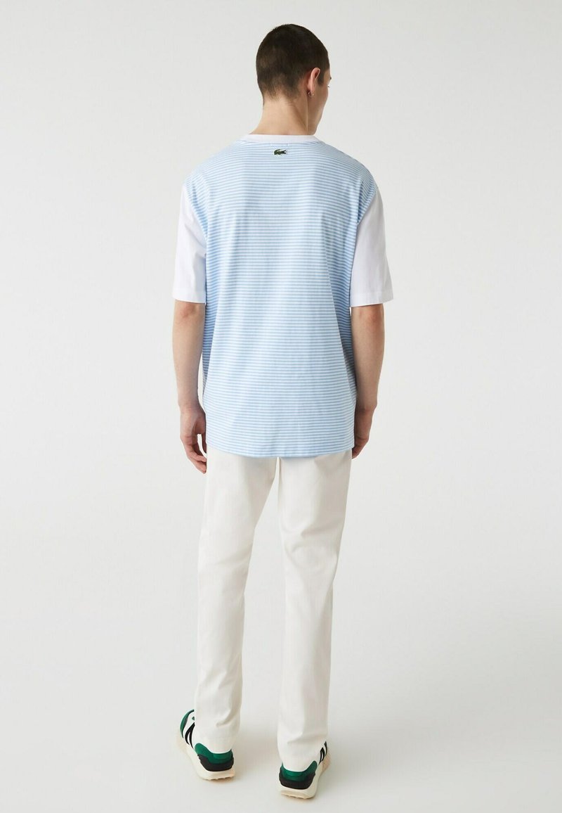 T-shirt a maniche corte con righe azzurre e bianche, con una sezione inferiore bianca e logo nero sul retro. Abbinato a pantaloni bianchi.