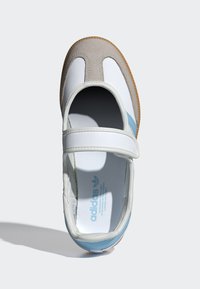 Biela a béžová topánka s modrým detailom, vybavená pásikom na suchý zips, zaoblenou špičkou a textúrovanou gumovou podrážkou. Vo vnútri je viditeľné logo.