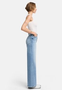 Jeans taille haute, coupe droite en denim bleu clair. Comprend des poches avant, des poches arrière plaquées et un design épuré et minimal. Fini plat.