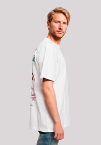 Weißes Baumwoll-T-Shirt mit kurzen Ärmeln, das auf der Rückseite farbenfrohe Grafiken zeigt, einschließlich Text, einem karierter Muster und einem Designmotiv.