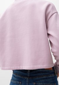 Felpa cropped di un delicato viola chiaro, realizzata in morbido misto cotone, con polsini e orlo a costine, abbinata a jeans blu a vita alta.