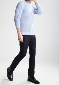 Jasnoniebieski sweter z prążkowanej dzianiny z długimi rękawami, w zestawie z ciemnymi spodniami w kratę i czarnymi sznurowanymi botkami, o gładkiej fakturze.