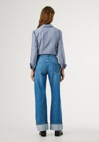 Blue and white striped long-sleeve shirt paired with high-waisted light blue wide-leg jeans, featuring rolled cuffs and back pockets.