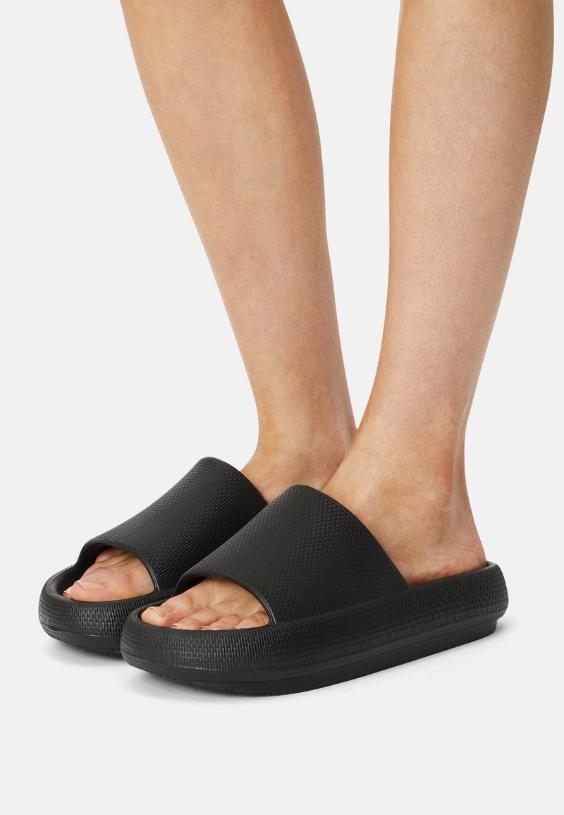 Sandales à glissière noires avec une tige texturée et un design large à bout ouvert. Elles disposent d'une semelle coussinée légèrement surélevée pour le confort.