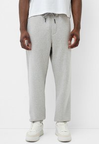 Graue Sweatpants mit elastischem Bund und Kordelzug, ausgestattet mit Seitentaschen. Tragen Sie sie mit weißen Turnschuhen, das Material wirkt weich und lässig.