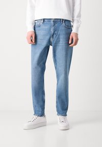 Lyseblå denimjeans med lige pasform, fem lommer og metaldetaljer, parret med hvide sneakers og en hvid sweatshirt.