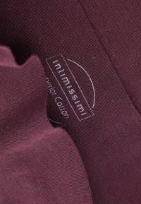 Burgundytyg med en slät yta som har en sydd kant. En präglad etikett visar varumärket i vitt på ena sidan.