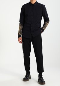 Czarna koszula z guzikami, z tkaniną w złoty wzór na rękawach, w zestawieniu z czarnymi spodniami o dopasowanym kroju i czarnymi butami. Slim fit; gładka tekstura.