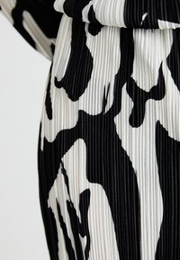 Tissu plissé en noir et blanc présentant des motifs abstraits de formes variées. La texture est légèrement brillante, mettant en valeur le mouvement du design.