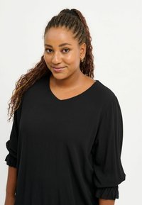Top nero a V con maniche a sbuffo tre quarti, realizzato in tessuto morbido, presenta una vestibilità comoda e delicate dettagli arricciati ai polsini.