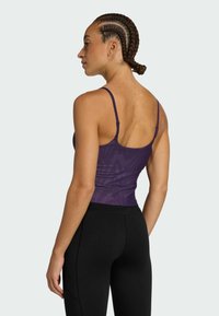 Purple athletic tank top with thin straps, featuring a geometric texture. Paired with black high-waisted leggings, showcasing a smooth finish.