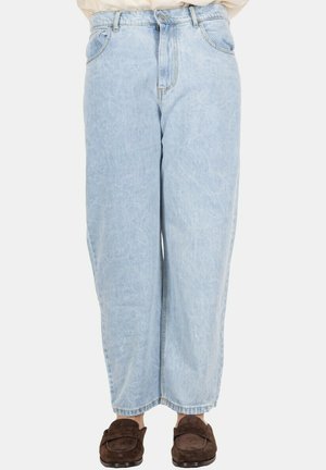 Jeans azzurri chiari a vita alta e gamba larga indossati con mocassini in suede marrone, mostrati dalla vita ai piedi su sfondo bianco.