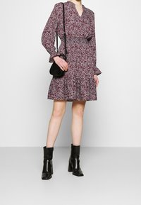 Blommönstrad klänning med långa ärmar, åtsittande midja och flerskiktad kjol i vinröd och vit. Matchas med svarta klackstövlar och en liten väska.