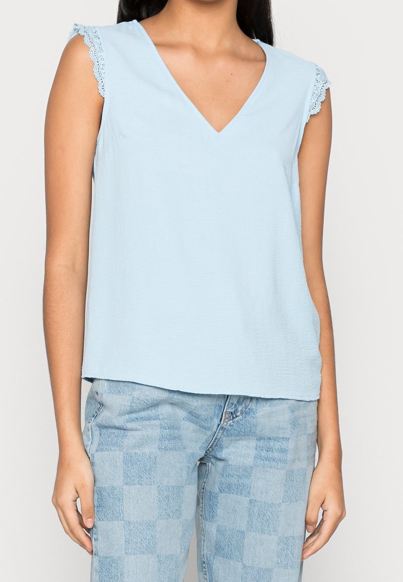Haut bleu clair sans manches avec un col en V et un bord en dentelle sur les épaules. Confectionné dans un tissu doux, avec une coupe décontractée et un design simple.