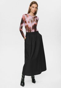 T-shirt à manches longues avec un motif abstrait rose et marron, associé à une jupe noire longueur cheville avec une taille élastique et des poches.