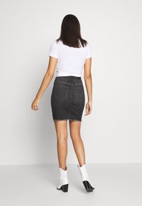 Falda lápiz de mezclilla oscura con dobladillo deshilachado, combinada con una camiseta blanca ajustada y botas blancas hasta el tobillo. Diseño sencillo, cintura de altura media.