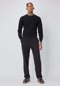 Pull noir à manches longues avec encolure ronde, assorti à un pantalon noir à taille élastique et des chaussures noires à semelle robuste. Textures lisses dans l'ensemble.