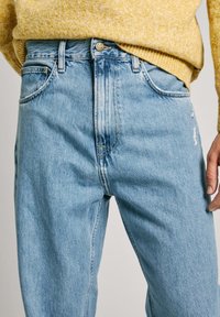 Svetlo modri denim kavbojki z udobnim krojem, ki vključujejo gumbasto zaponko, pet žepov in rahlo obrabljen videz tkanine.