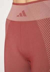 Leggings en tissu rouge sobre, dotés d'une taille haute texturée et à motifs, avec un design à rayures discrètes sur la partie inférieure de la jambe.