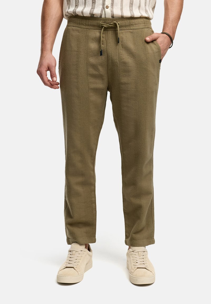 Pantalones ligeros de color verde oliva, hechos de tejido texturizado, con cintura de cordón y bolsillos laterales, combinados con zapatillas beige.
