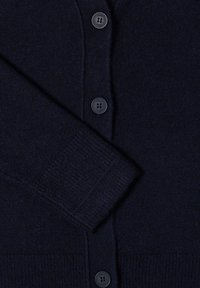 Mörkblå stickad cardigan med knäppning fram, ribbade ärmslut och en slät textur. Har fyra svarta plastknappar.