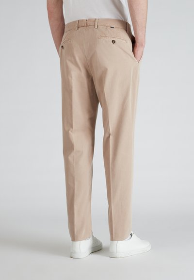 Pantaloni di cotone beige con taglio dritto, dotati di due tasche posteriori con bottoni e una texture liscia. Abbinati a sneaker bianche.