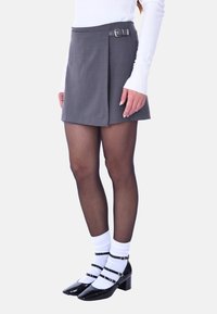 Gonna mini grigia plissettata con dettaglio in argento, abbinata a collant neri trasparenti e scarpe con tacco a blocco in pelle lucida nera. Calzini bianchi inclusi.