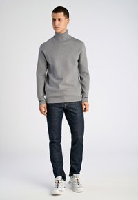 Grauer Rollkragenpullover aus strukturiertem Material, kombiniert mit dunkelblauen Jeans und weißen Sneakers mit bunten Akzenten.