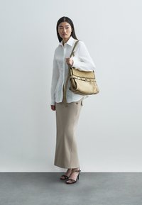 Μπεζ δερμάτινη τσάντα ώμου με δομημένο σχέδιο, που διαθέτει φαρδιά λουράκι, ασημένια εξαρτήματα και διακριτικές λεπτομέρειες ραφής.